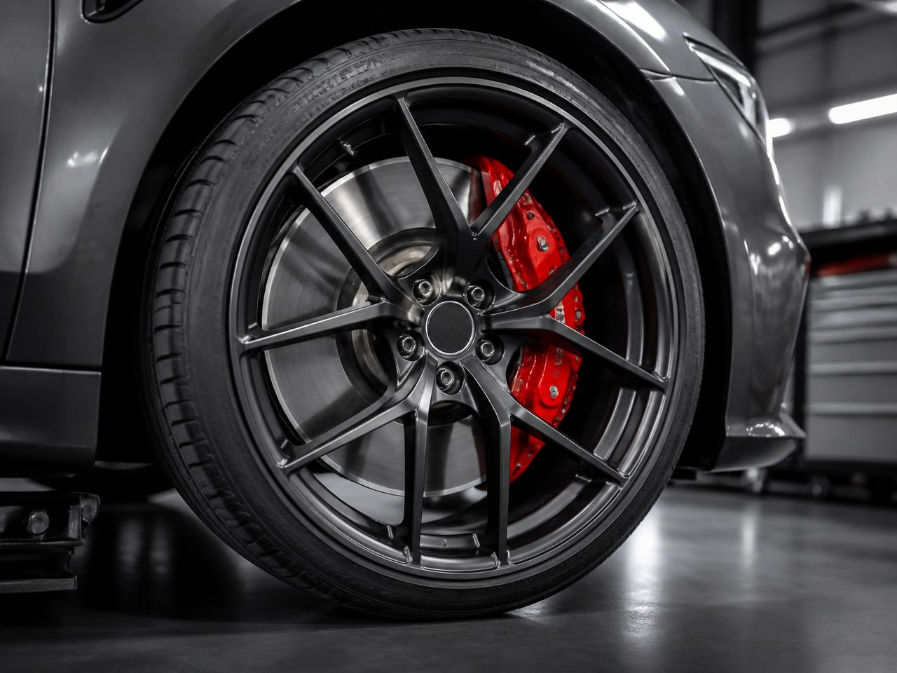 European sedan wheel with red multi-piston caliper and smooth rotor behind a dark forged wheel